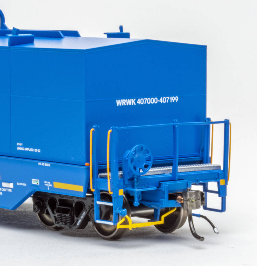 Color photo showing B end details on modern HO scale coil gondola with hood painted blue with white and yellow graphics and black trucks on white background. 
